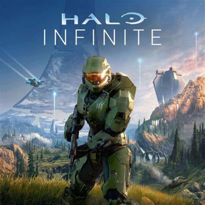Halo Infinite's Master Chief shoots enemies from behind a shield.